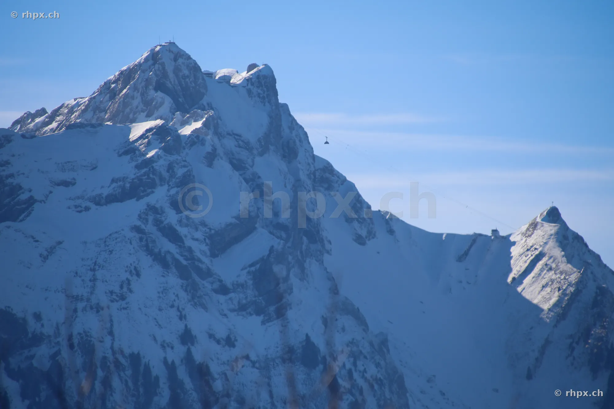 The snow-covered summit of Mount Pilatus near Lucerne with a small gondola in the sky.