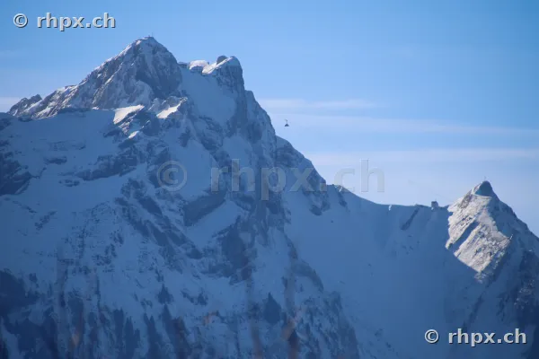 Der verschneite Gipfel des Pilatus bei Luzern mit einer kleinen Gondel am Himmel.