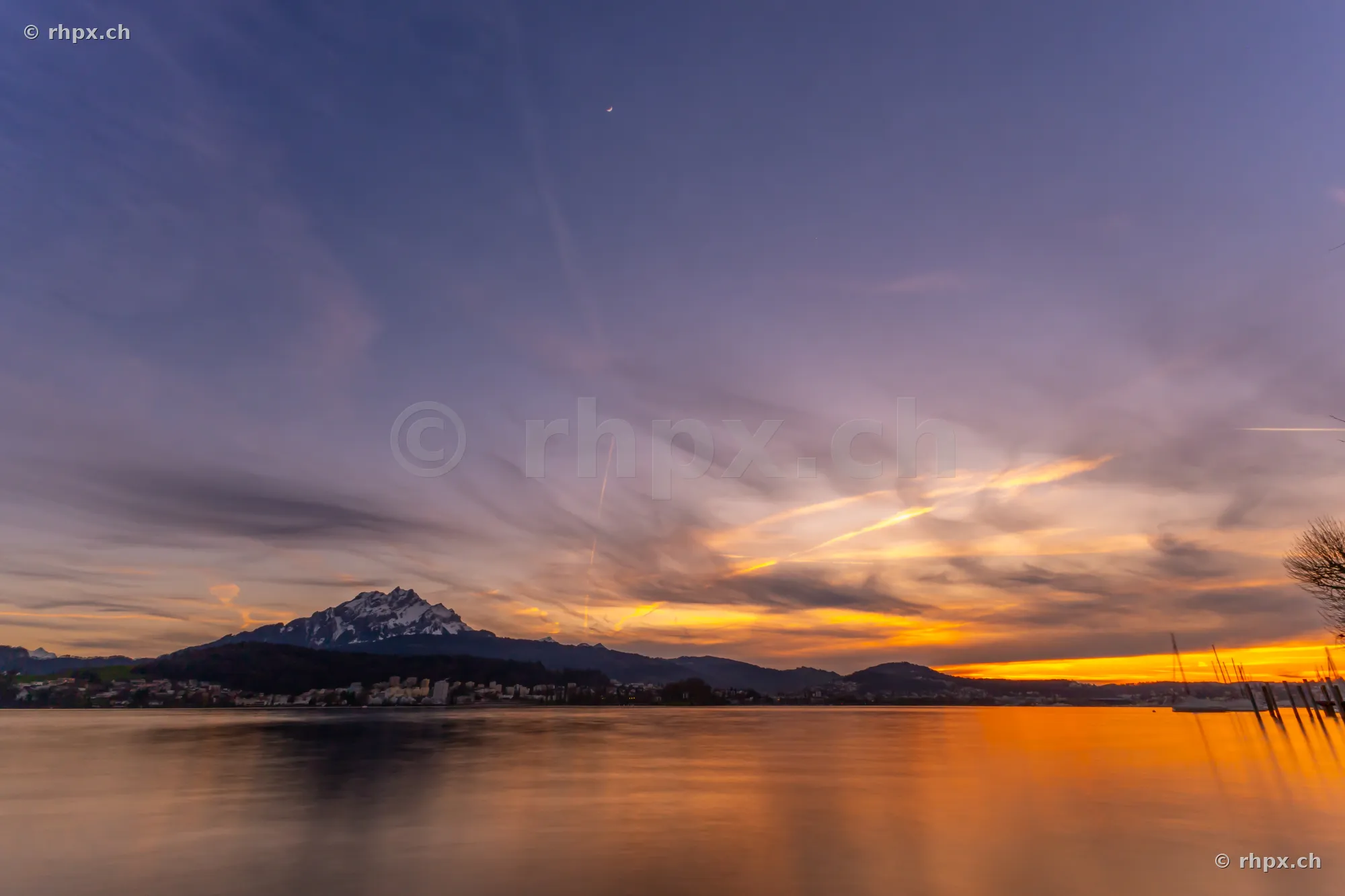 View of Lake Lucerne and Mount Pilatus at dusk with a thin crescent moon in the sky.