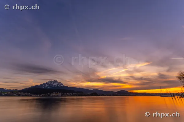 View of Lake Lucerne and Mount Pilatus at dusk with a thin crescent moon in the sky.