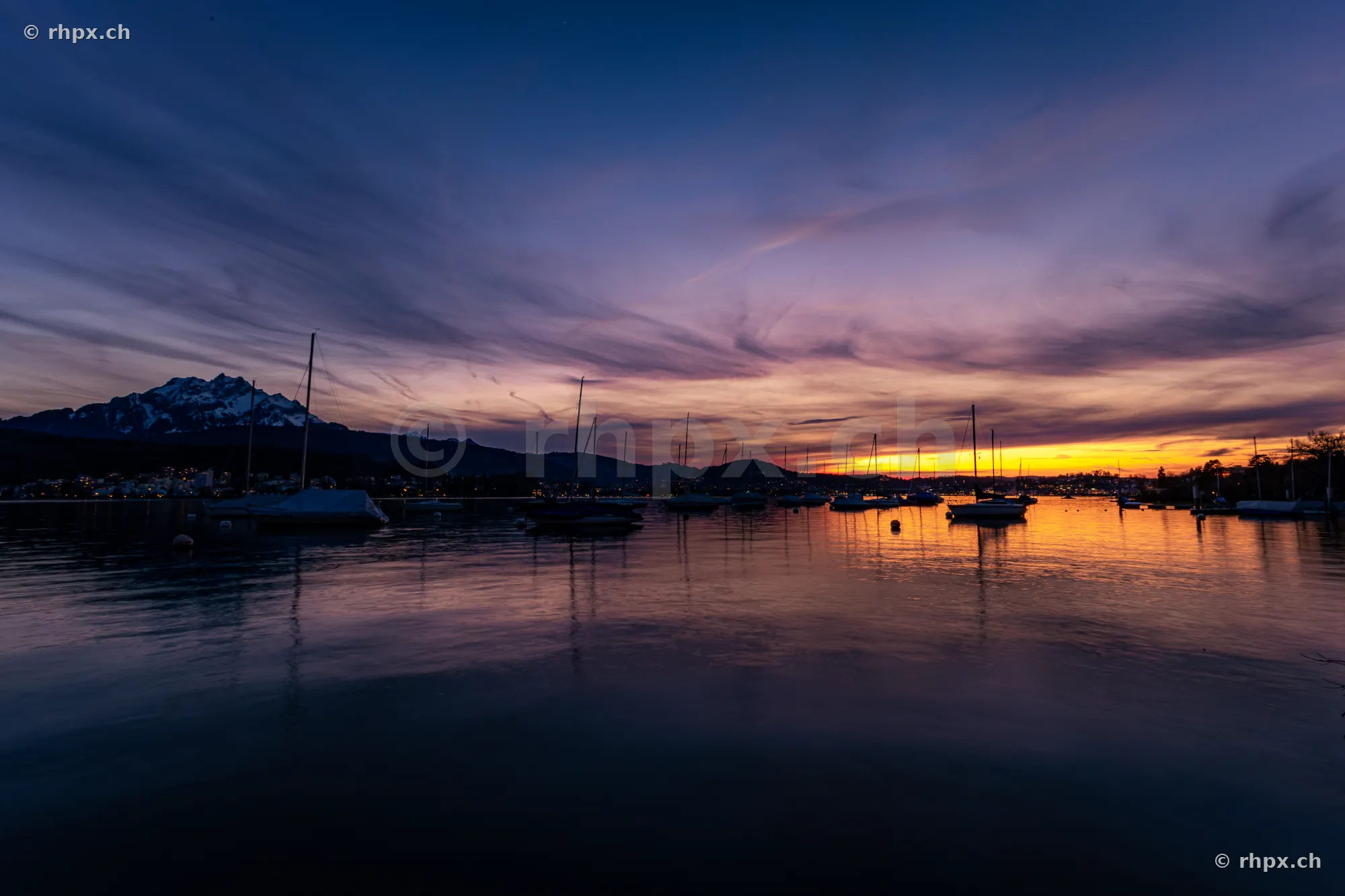 Silhouettes of sailboats on Lake Lucerne with Mount Pilatus at sunset