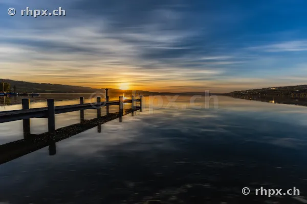 Holzsteg ragt in den ruhigen Sempachersee unter einem orangefarbenen Abendhimmel