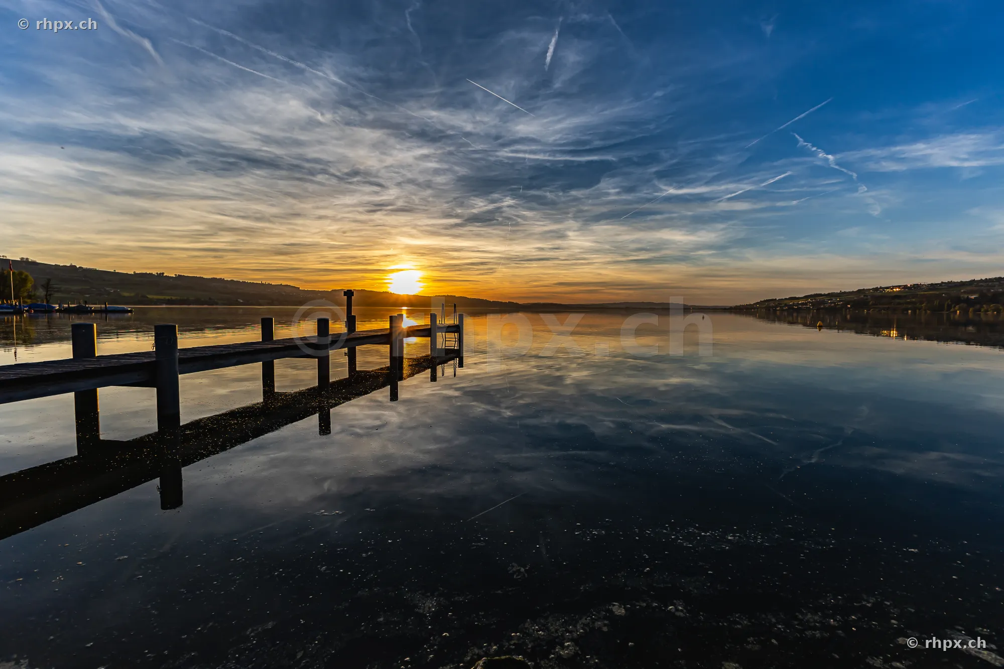Ein hölzerner Steg führt in den ruhigen Sempachersee unter einem von Wolken durchzogenen Abendhimmel.