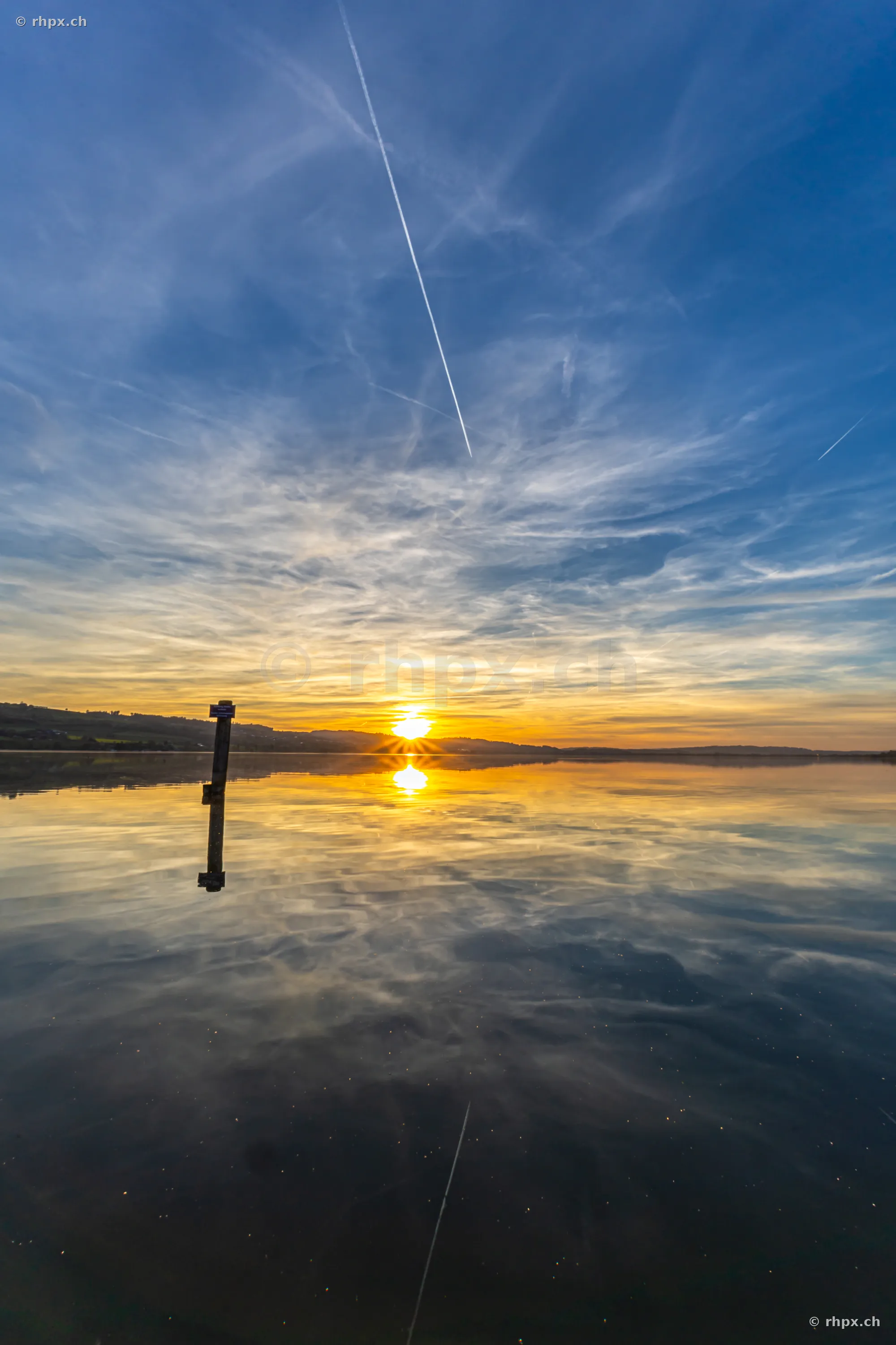 Sonnenuntergang über dem Sempachersee mit einem einzelnen Pfahl im Wasser