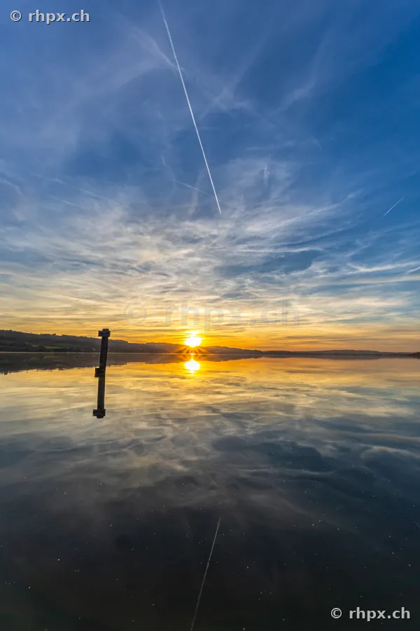 Sonnenuntergang über dem Sempachersee mit einem einzelnen Pfahl im Wasser