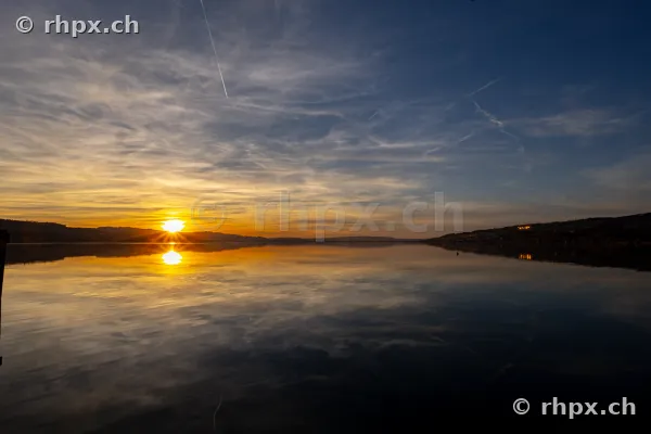Sonne tief über dem ruhigen Sempachersee bei Dämmerung
