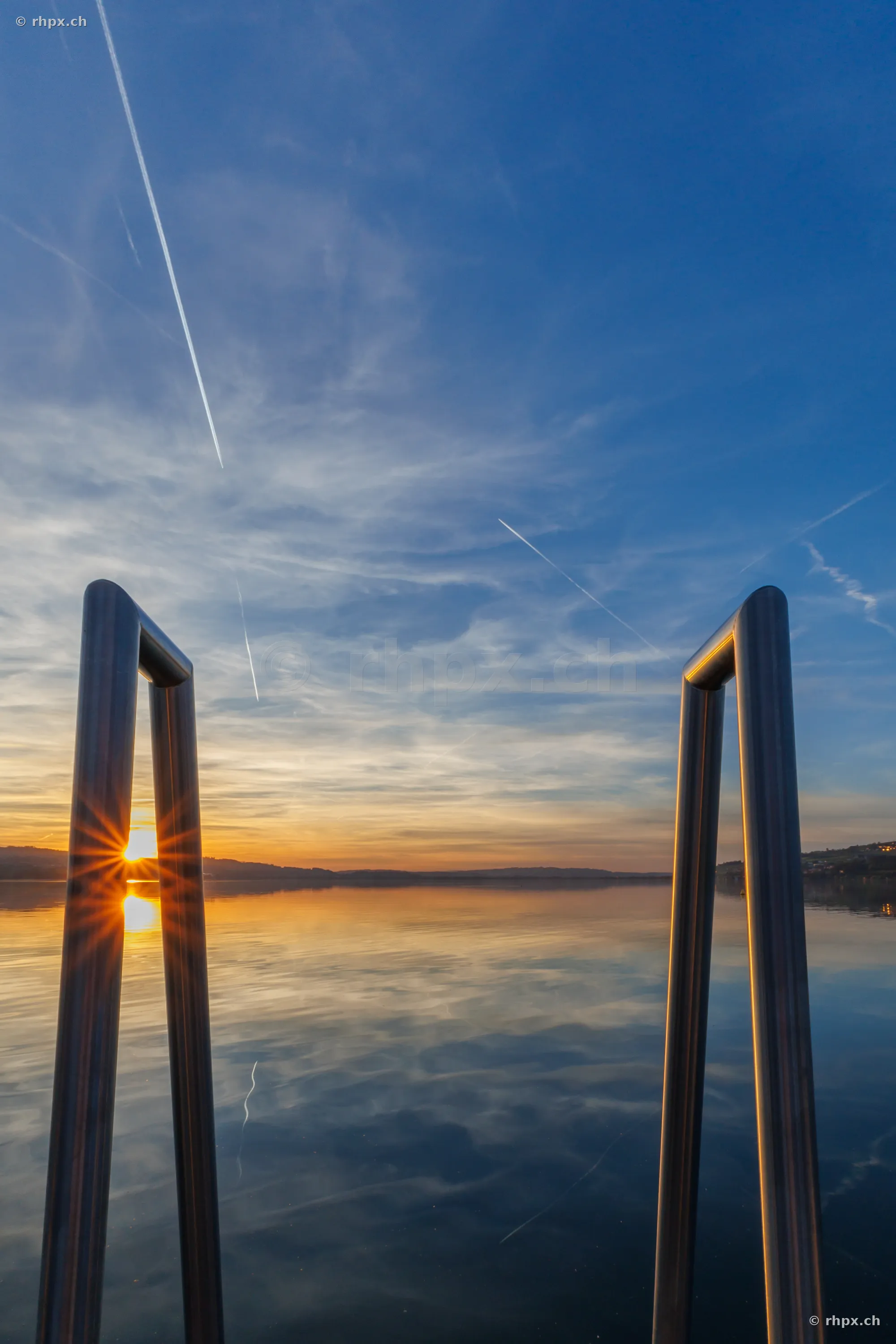 Blick durch eine metallene Badeleiter über den ruhigen Sempachersee beim Sonnenuntergang