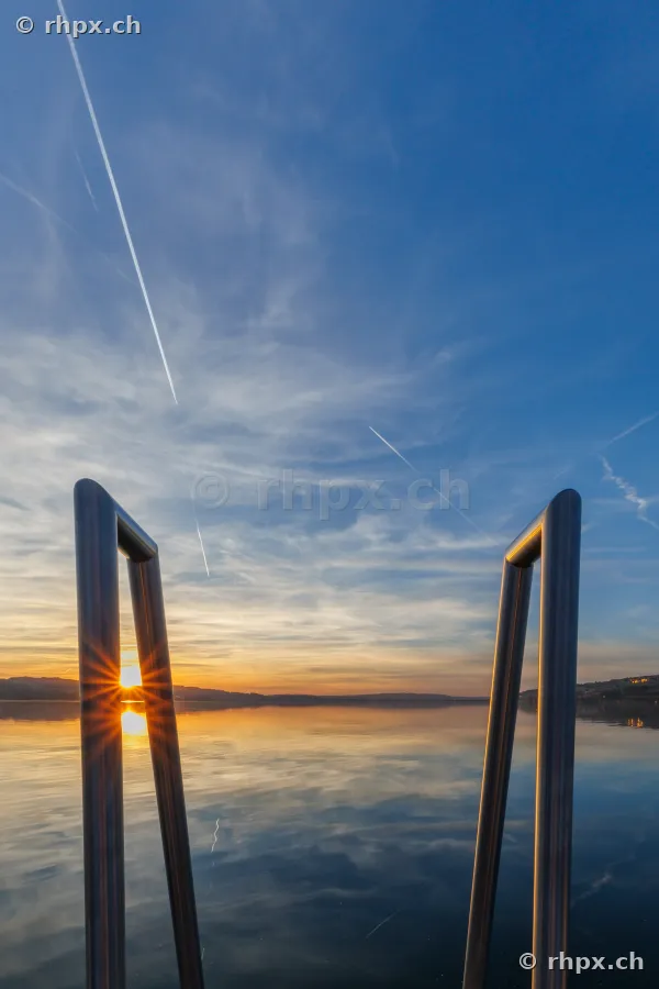 Blick durch eine Badeleiter auf den Sempachersee bei Sonnenuntergang
