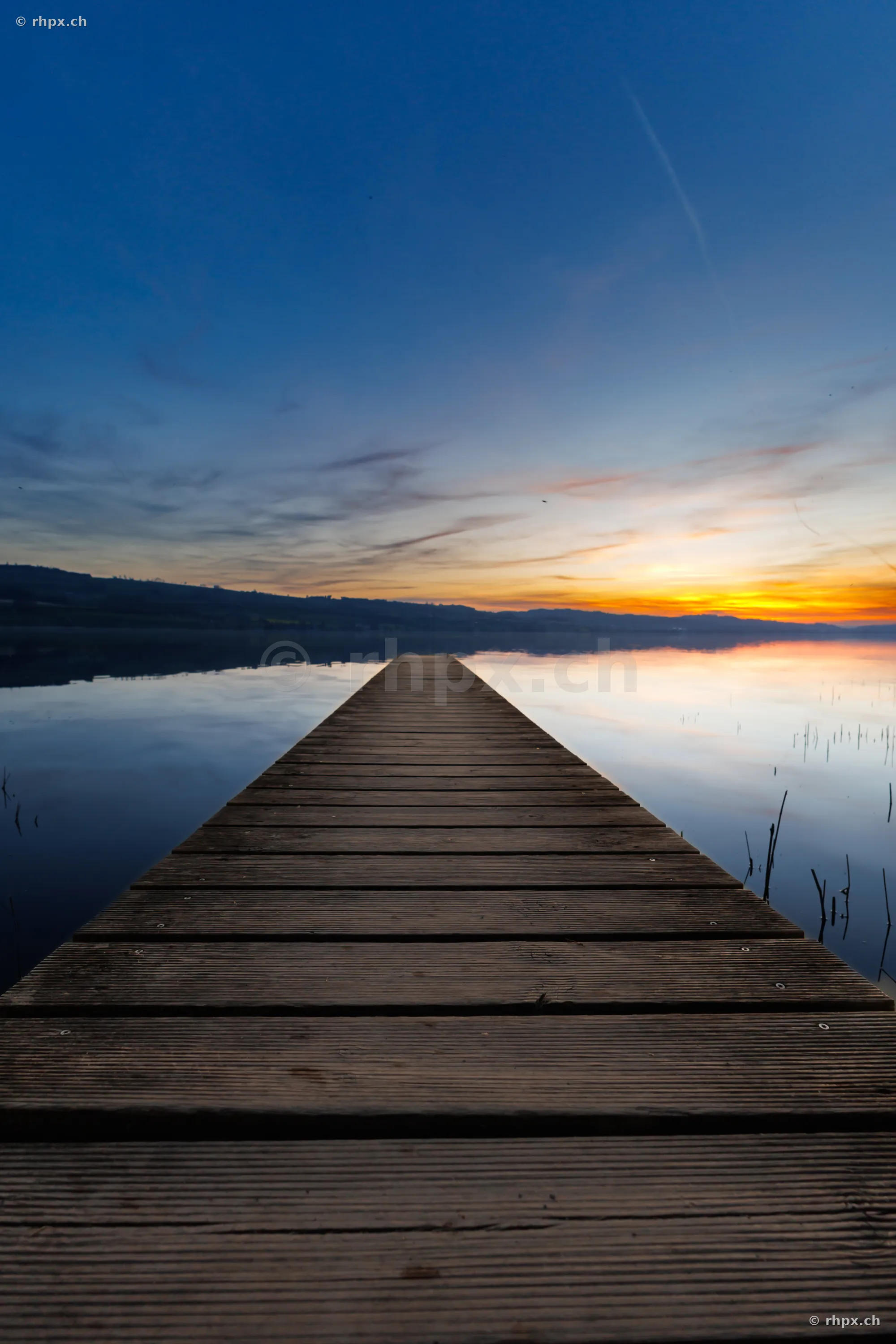 Holzsteg der in den ruhigen Sempachersee führt bei abendlicher Stimmung