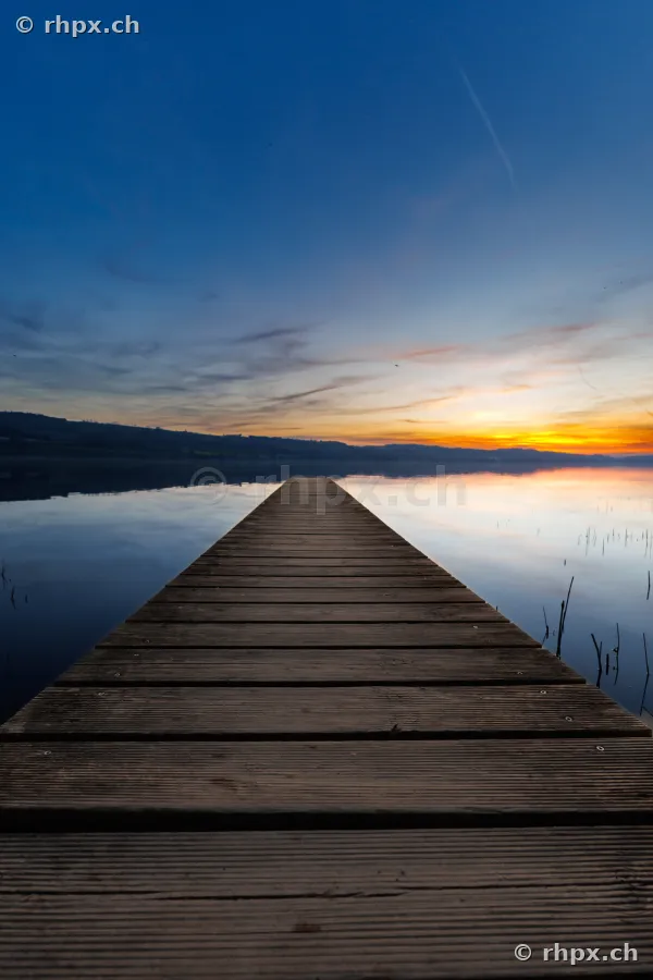 Holzsteg der in den ruhigen Sempachersee führt bei abendlicher Stimmung