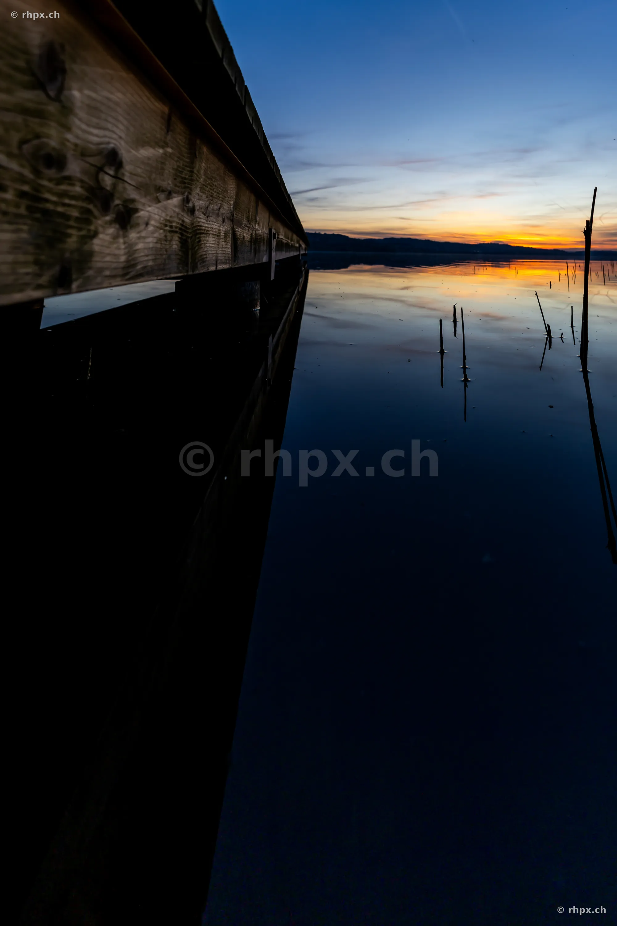 Blick entlang eines hölzernen Bootsstegs auf den ruhigen Sempachersee während des Sonnenuntergangs