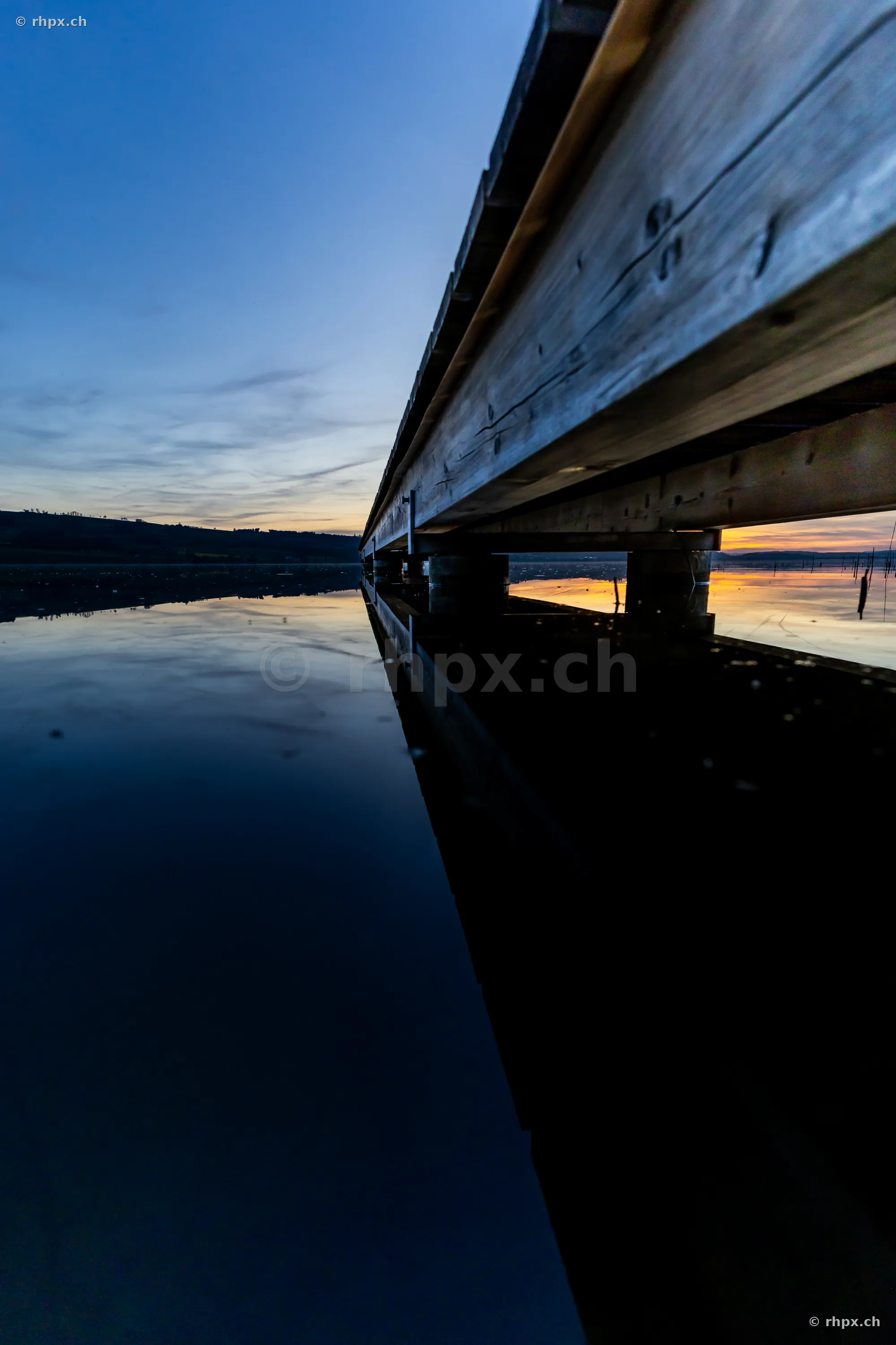 View under a wooden pier at Lake Sempach with reflection in the water at dusk