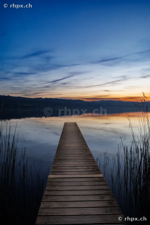Ein schmaler Holzsteg führt in den ruhigen Sempachersee während des Sonnenuntergangs