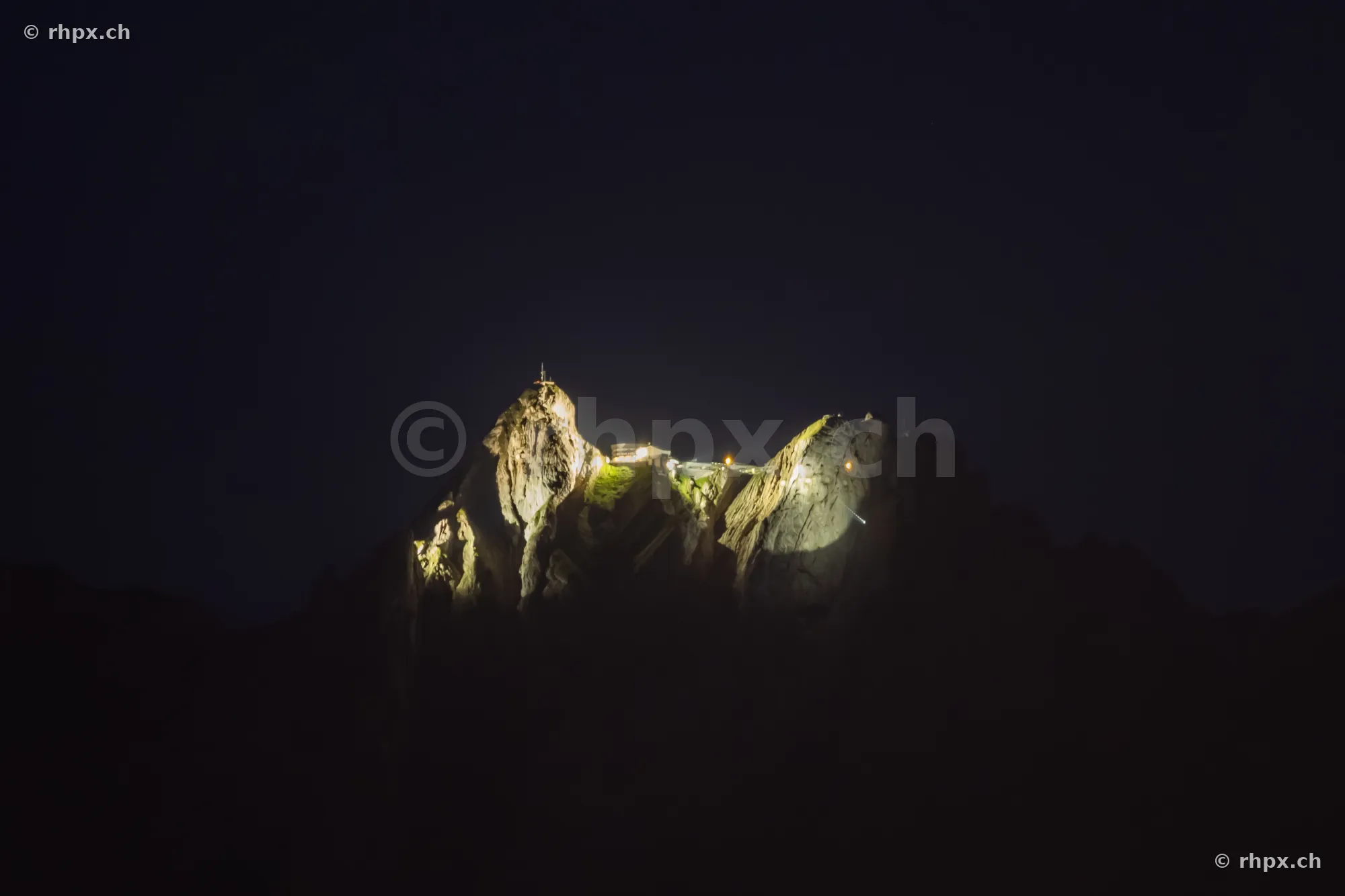 The illuminated summit of Mount Pilatus at night against a dark sky.
