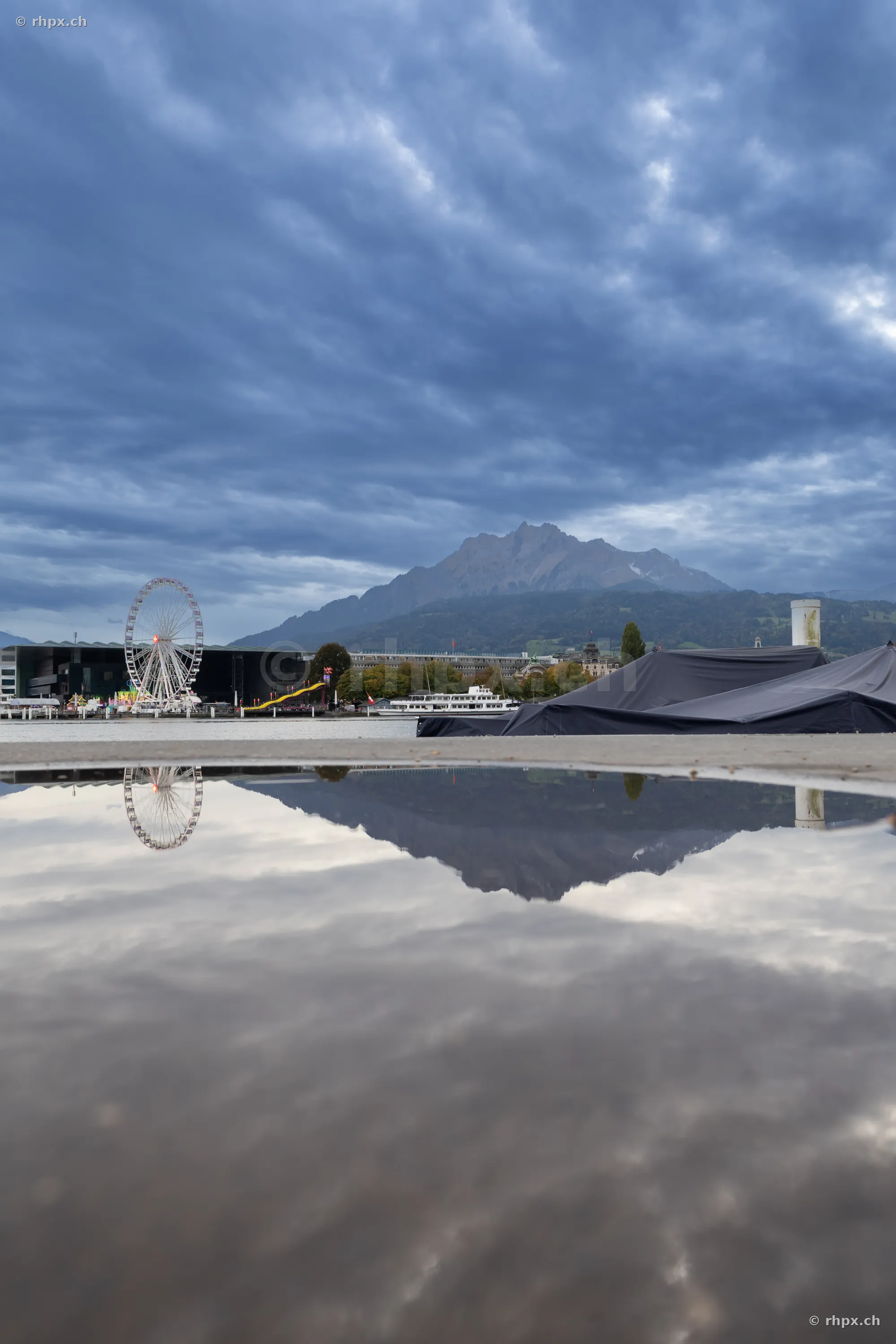 Ferris wheel and Mount Pilatus reflected in a puddle on the shore of Lake Lucerne.