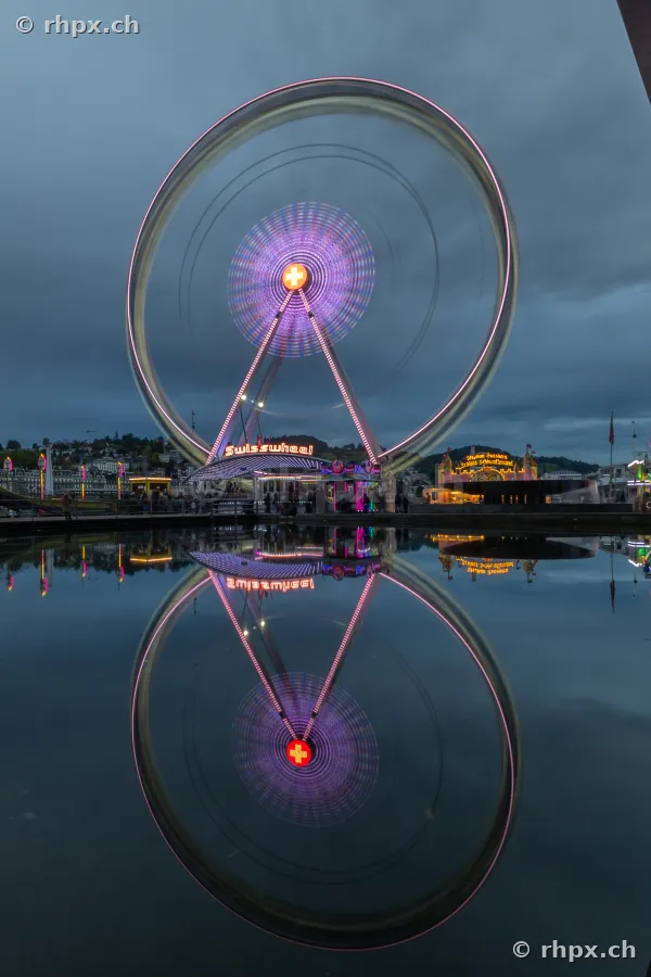 Das Riesenrad Swisswheel bei Dämmerung am Seeufer in Luzern, gespiegelt in der Wasseroberfläche.