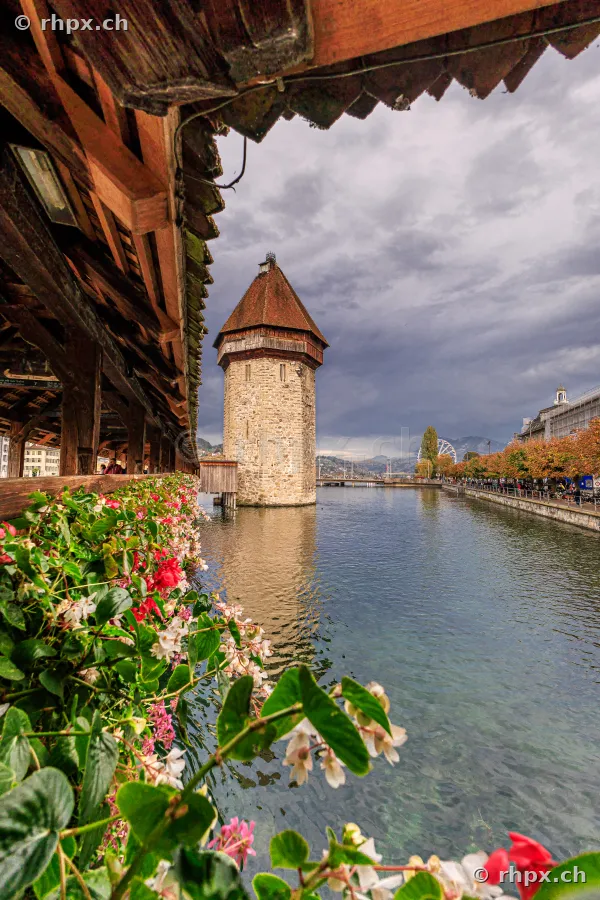 View through the interior of the Chapel Bridge towards the Wasserturm in Lucerne under a cloudy sky.