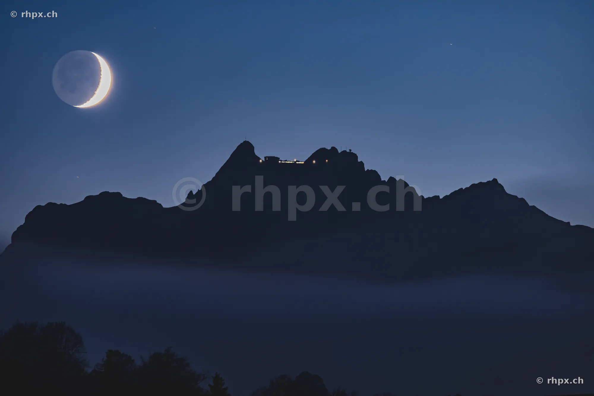 Crescent moon above the mist-covered Pilatus summit at night