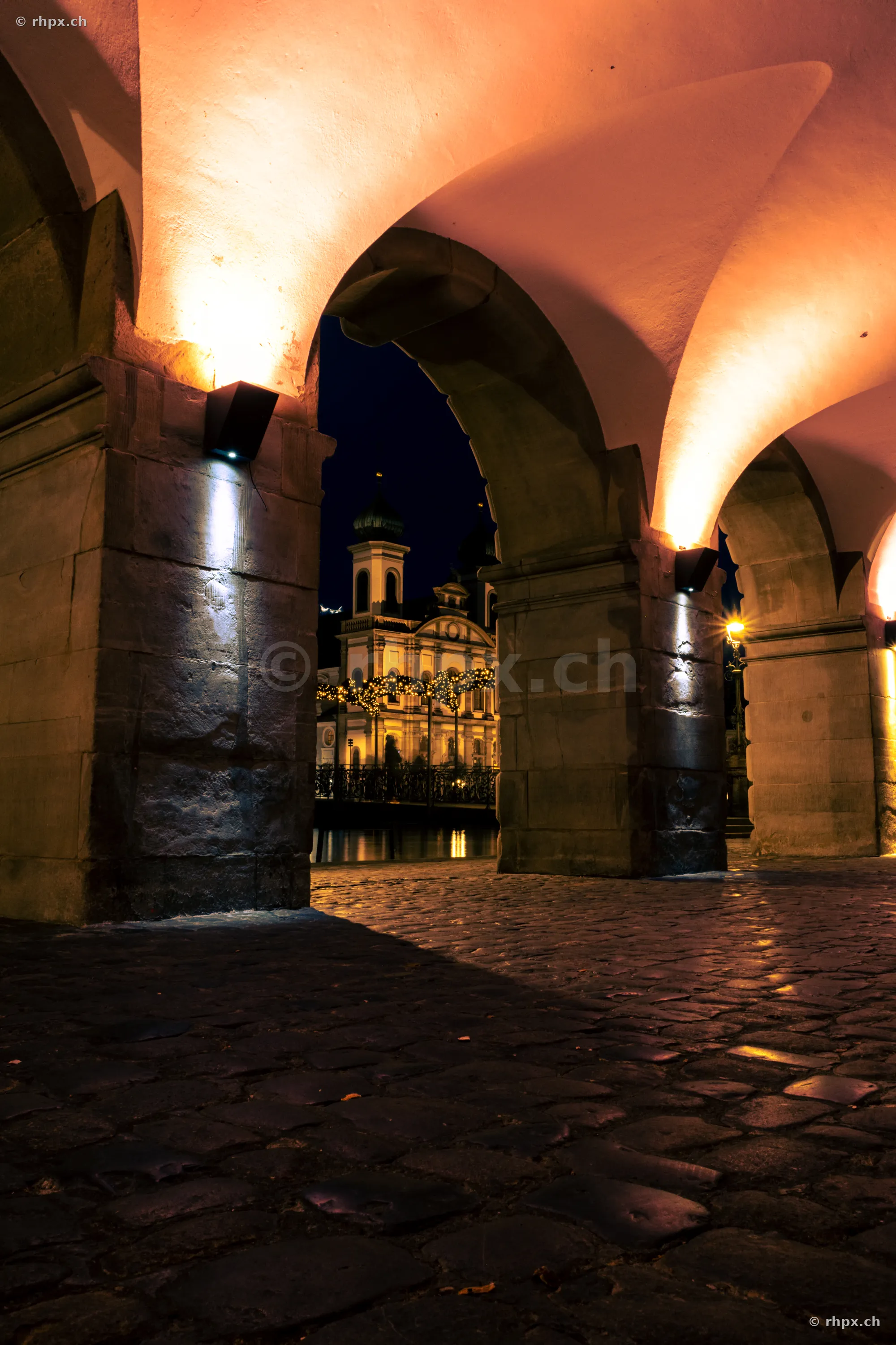 Blick durch die nächtlichen Rathaus-Arkaden auf die weihnachtlich beleuchtete Jesuitenkirche in Luzern