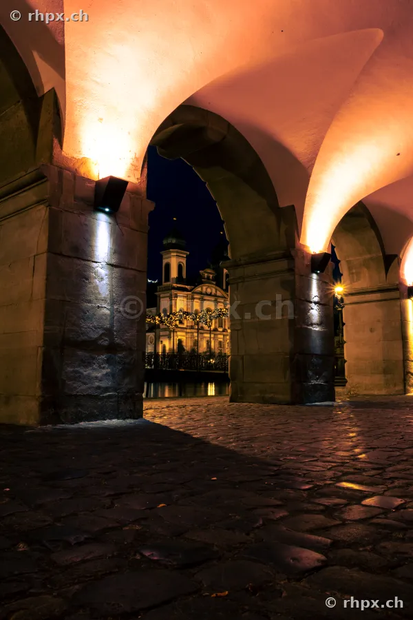 View through the nightly Rathaus arches towards the illuminated Jesuit Church in Lucerne during Christmas