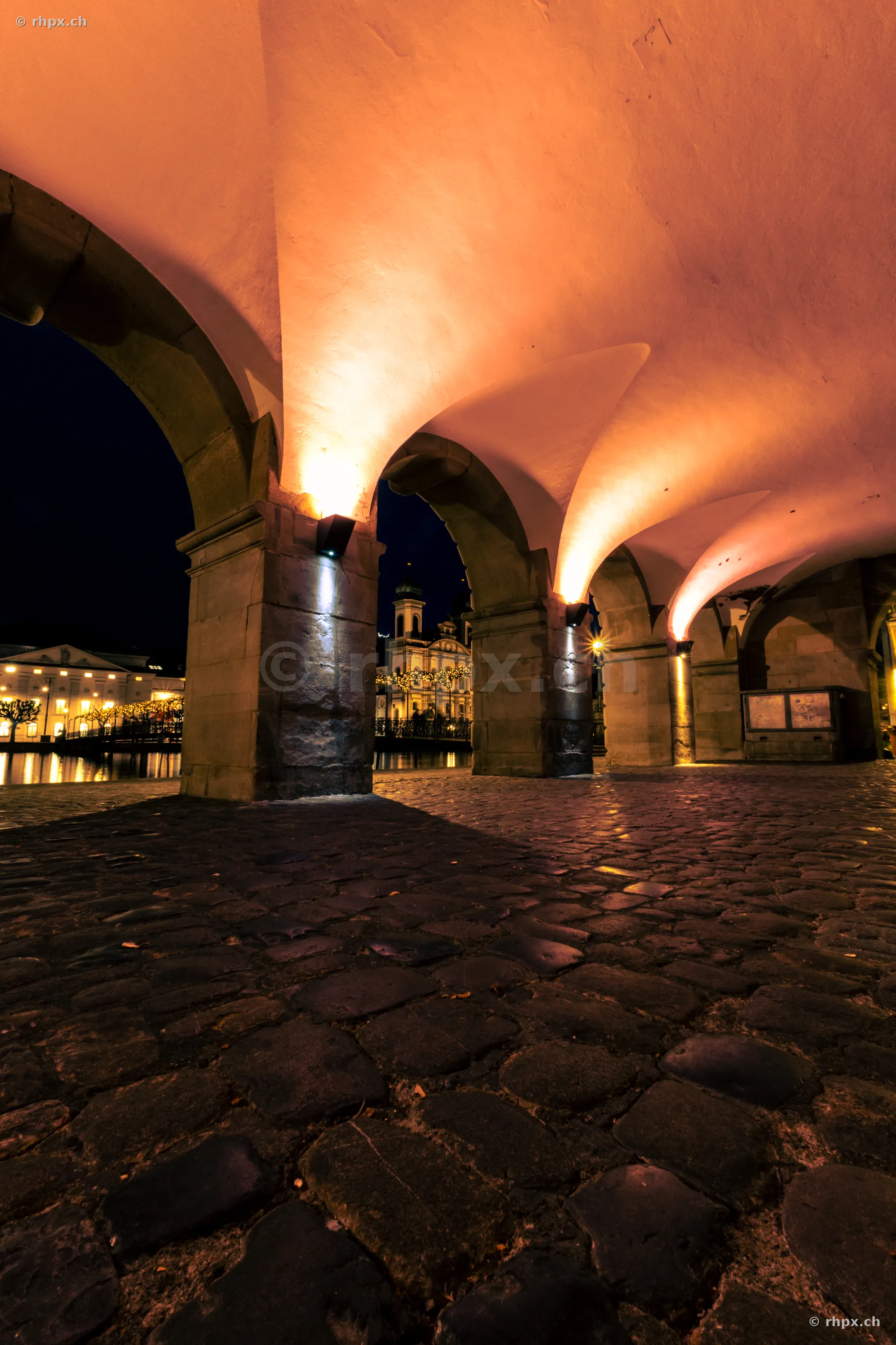 Blick durch die nächtlichen Rathaus-Arkaden auf die weihnachtlich beleuchtete Jesuitenkirche in Luzern