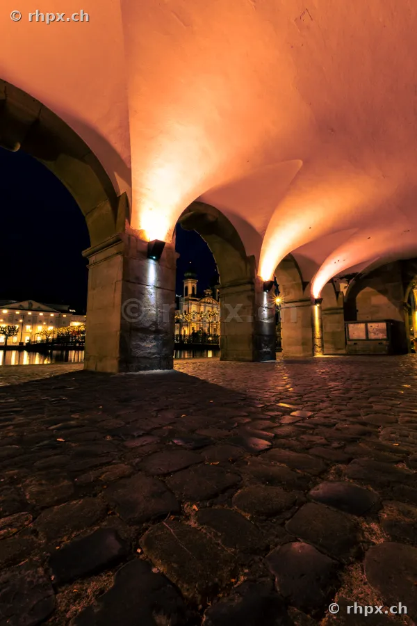 View through the nightly town hall arches towards the Christmas-lit Jesuit Church in Lucerne