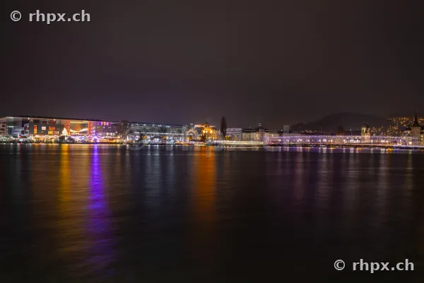 Nächtlicher Blick auf das weihnachtlich beleuchtete Seebecken in Luzern mit Spiegelungen im Wasser.