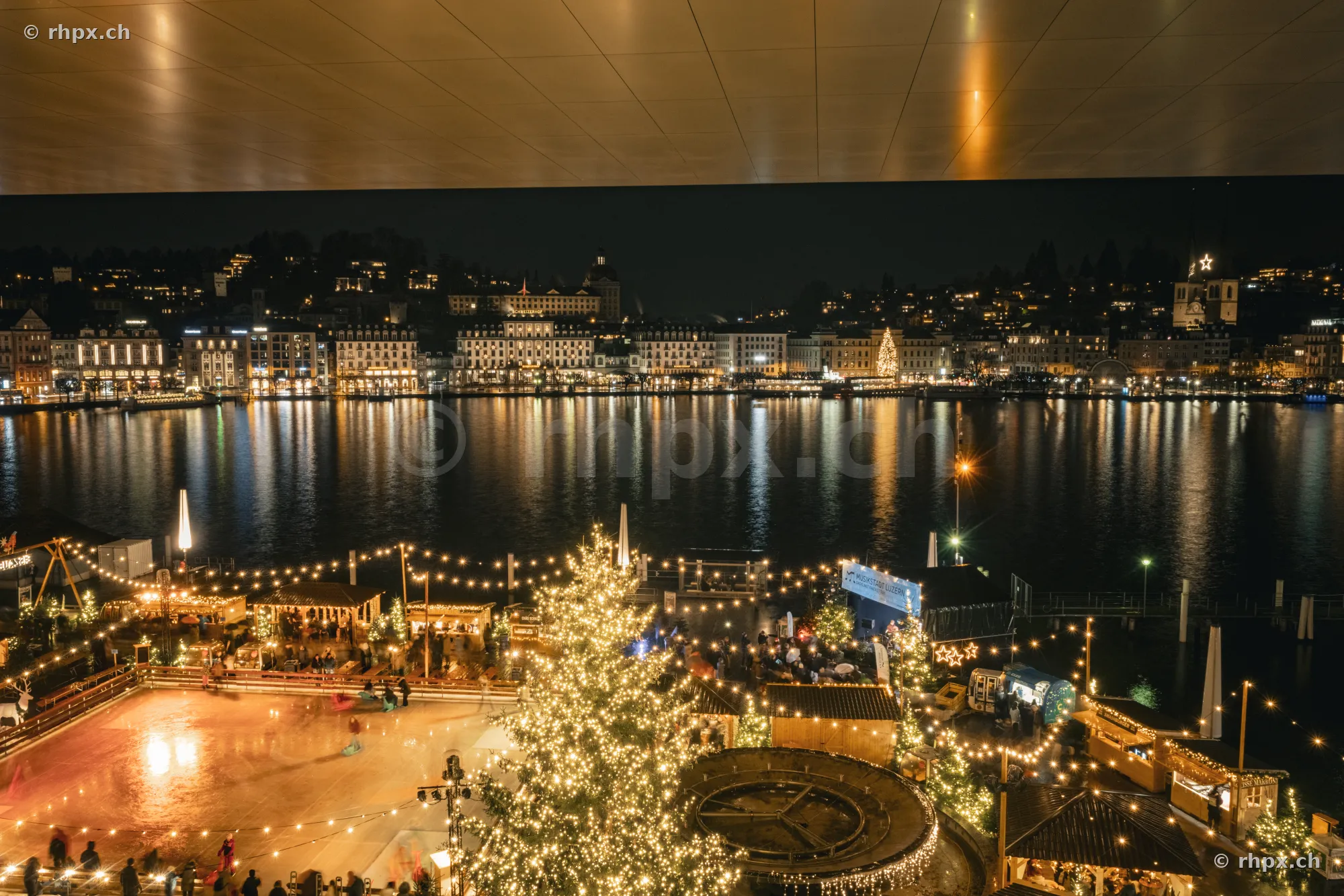 Nächtlicher Blick auf das beleuchtete Luzerner Seebecken mit Eisfeld und Weihnachtsbaum im Vordergrund