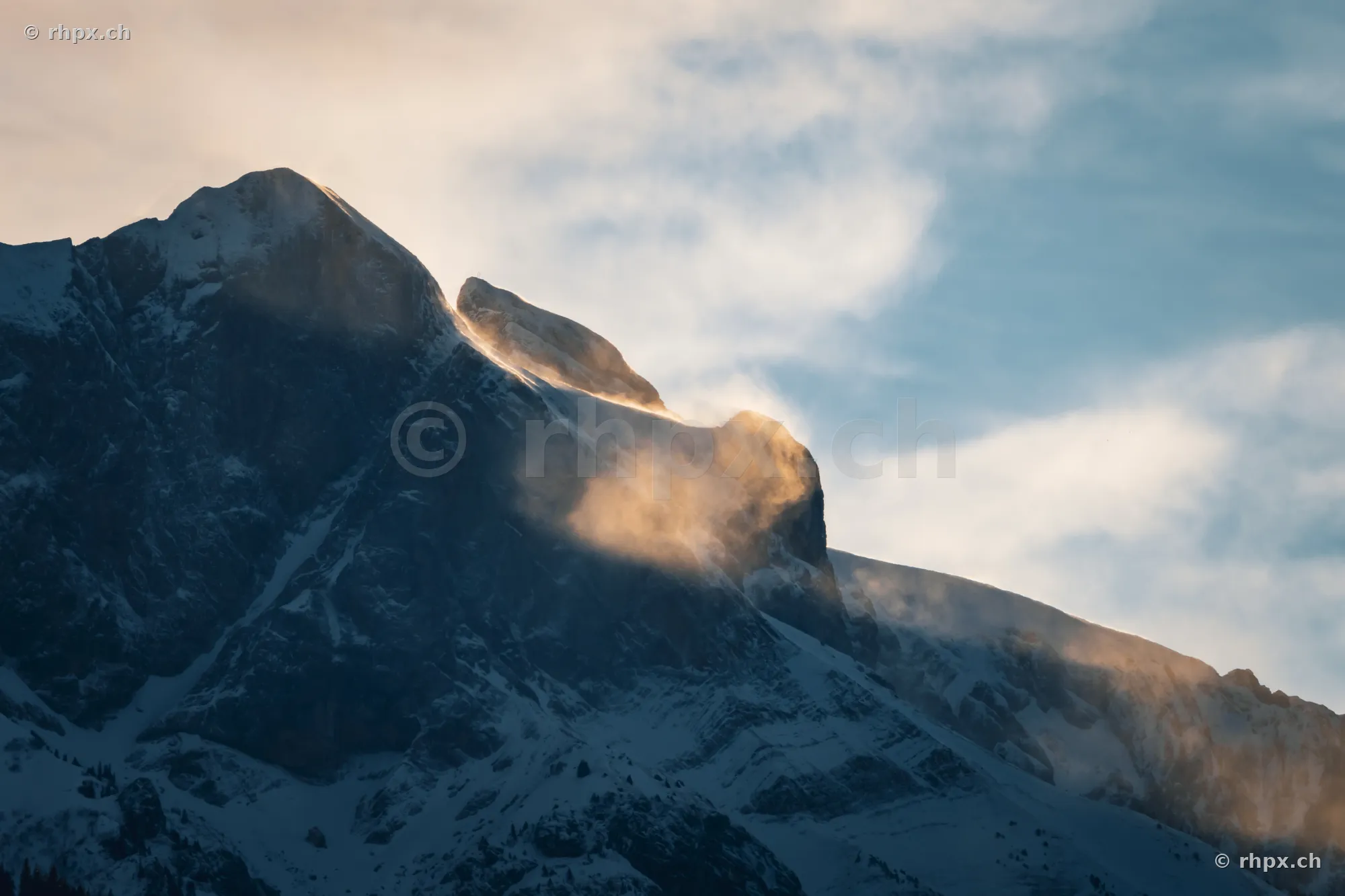 Detail view of the snow-covered Eiger North Face in the soft light of the setting sun with rising clouds.