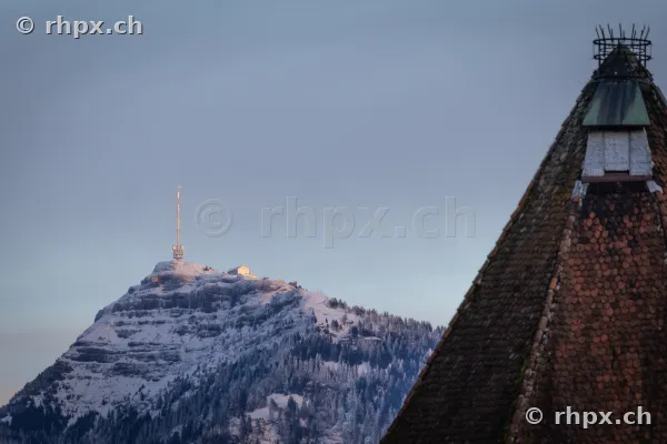 Snow-covered Rigi summit in the background and a pointed tiled roof of the Kapellbrücke in the foreground.
