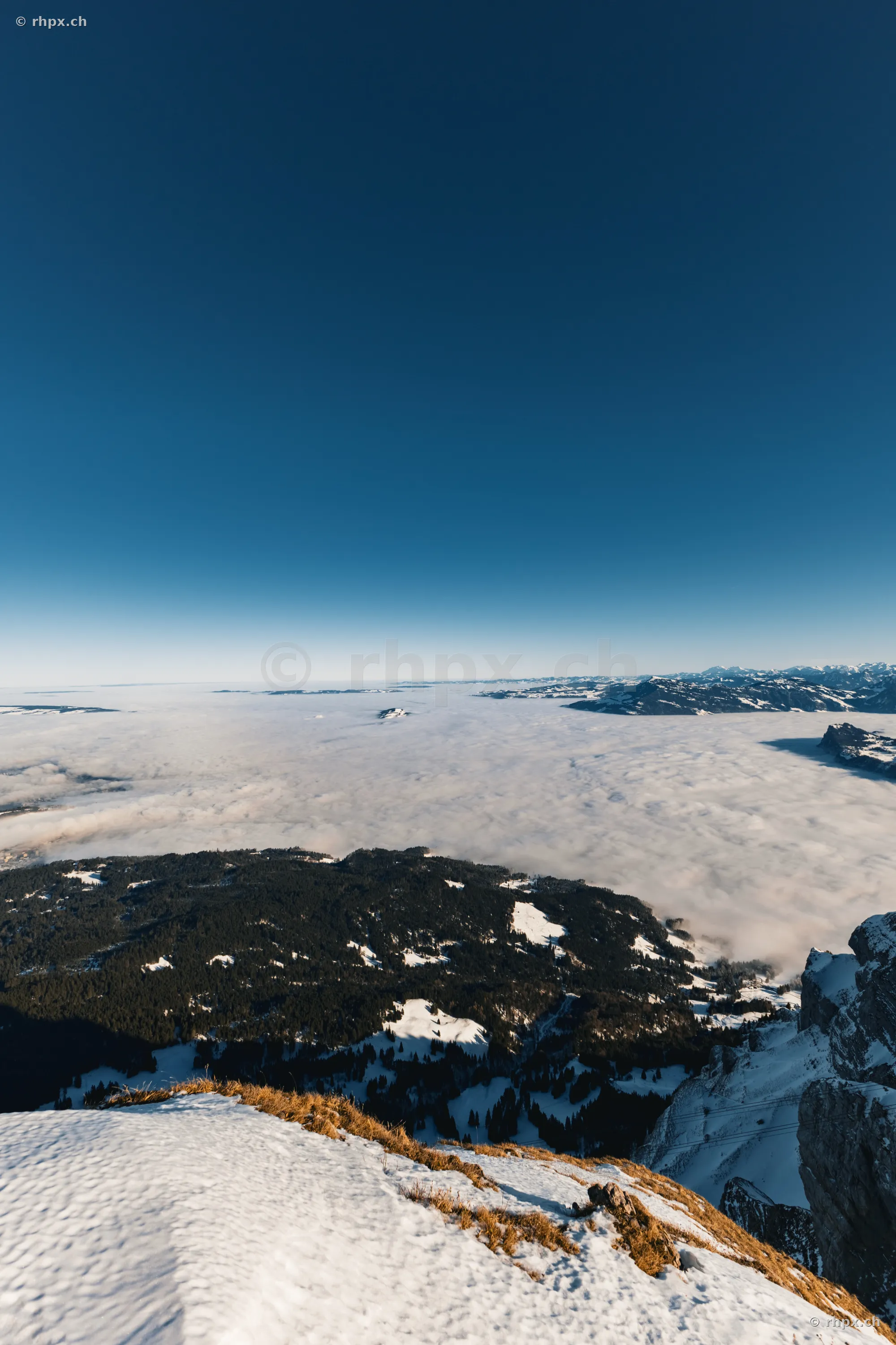 View from the snow-covered summit of Mount Pilatus looking over a sea of clouds under a clear blue sky.