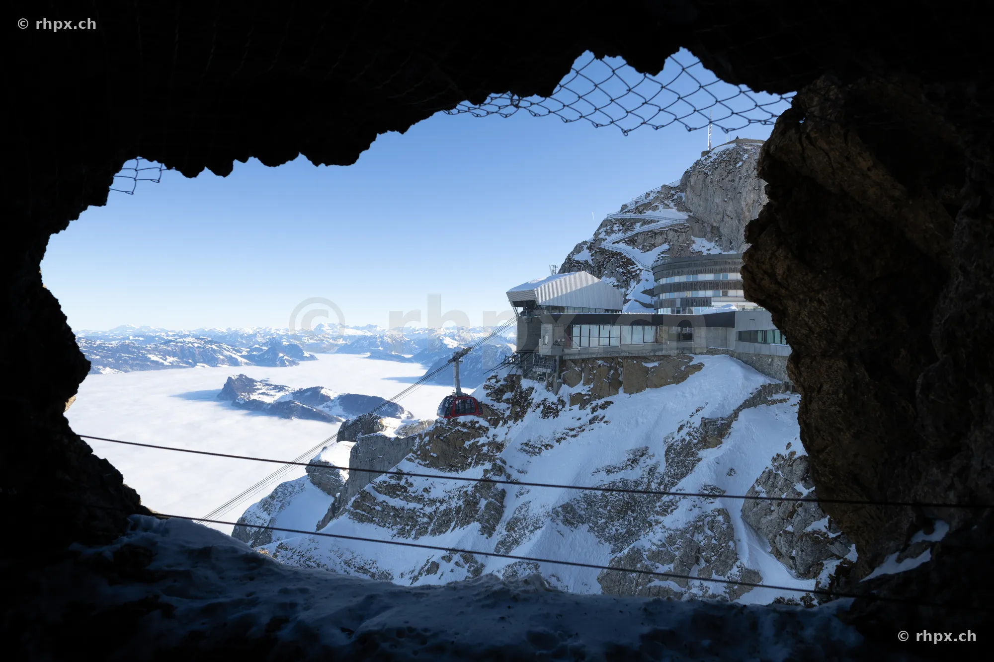 Blick durch eine Felsöffnung auf die Gipfelstation und den Pilatus im Winter