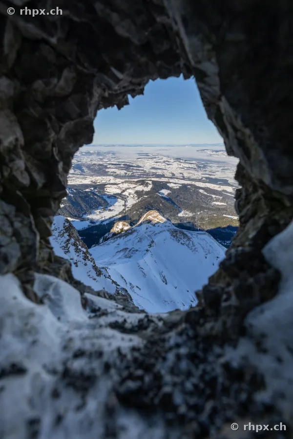 View through a rock opening onto the snow-covered summit region of Mount Pilatus