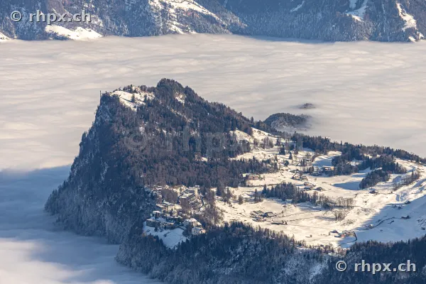 Luftaufnahme des verschneiten Bürgenstocks mit Hotellerie über einer tief liegenden Nebeldecke.