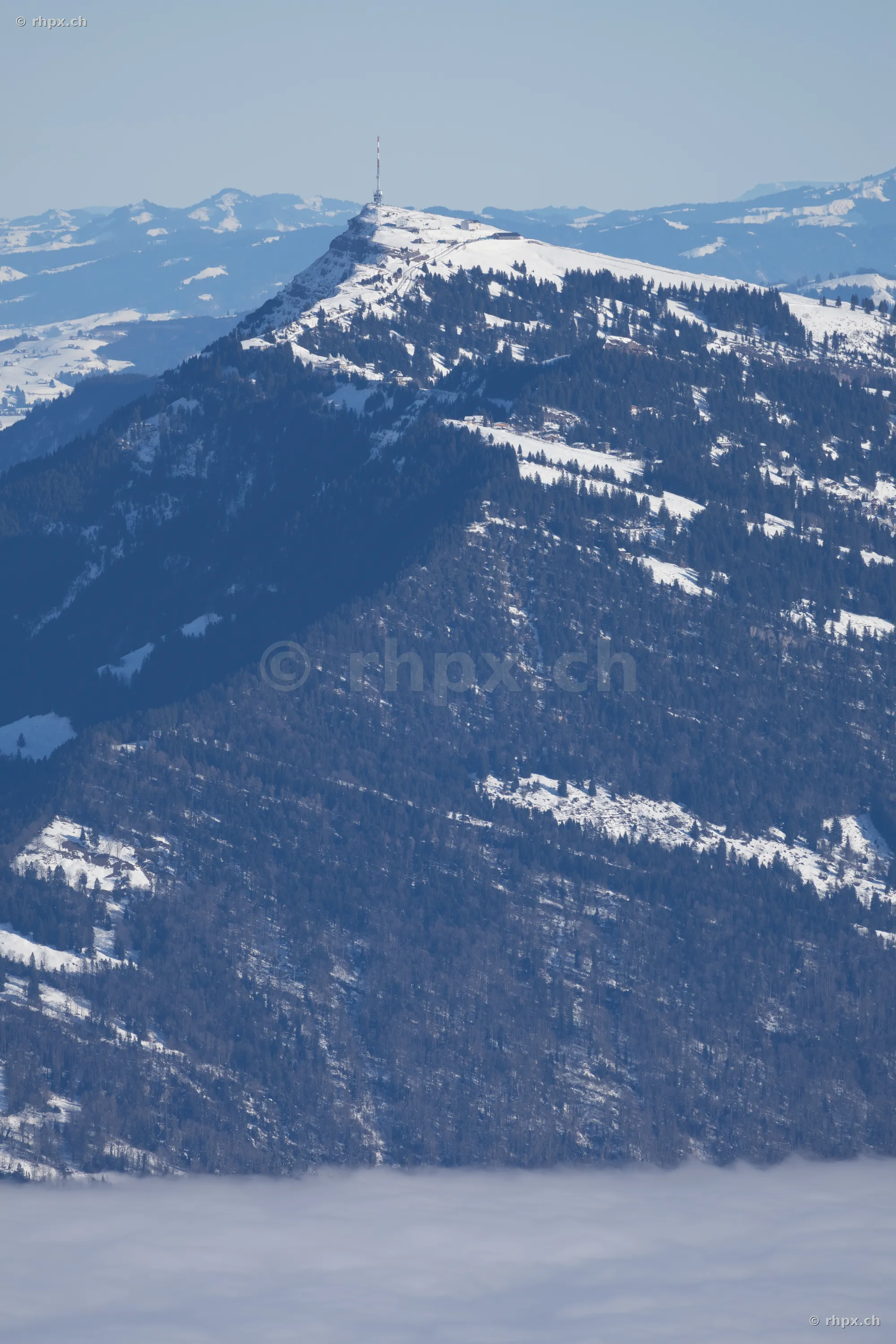 Blick auf den schneebedeckten Gipfel des Rigi mit Sendemast über einer Nebeldecke