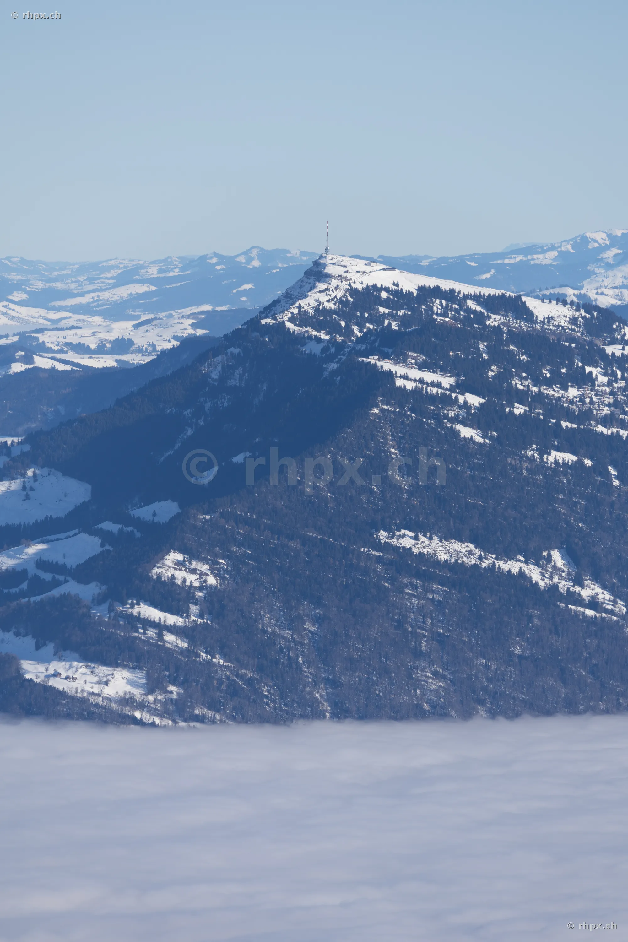 Blick auf den verschneiten Rigi Gipfel mit Sendeturm über einer dichten Nebeldecke.
