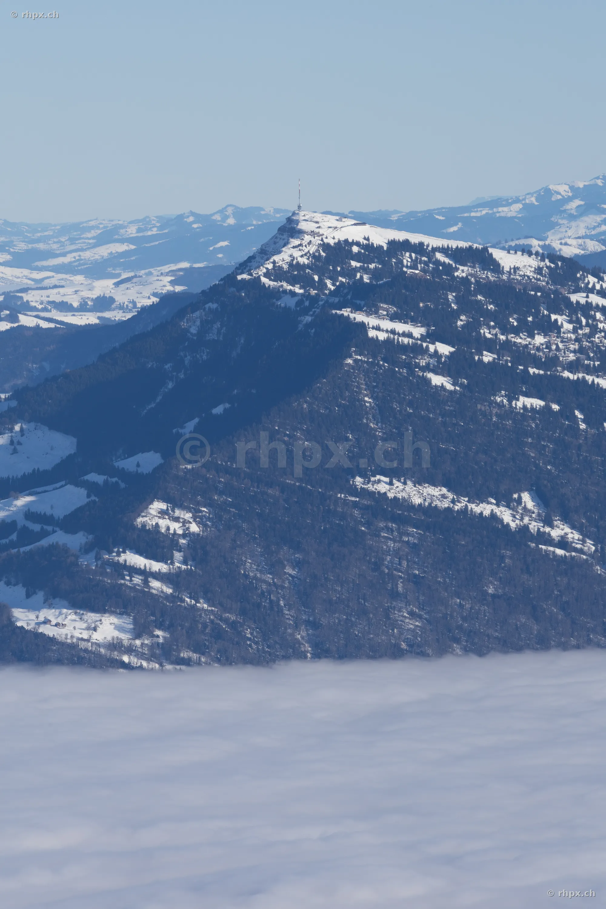 The snow-covered summit of Mount Rigi with a transmission tower rising above a dense layer of fog.