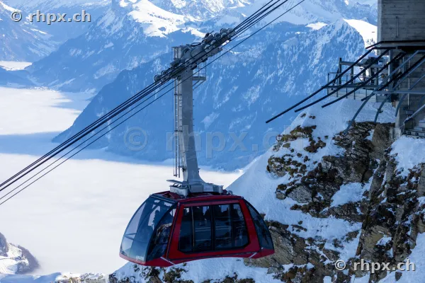 Rote Seilbahnkabine Dragon Ride fährt am schneebedeckten Pilatus über dem Nebelmeer.