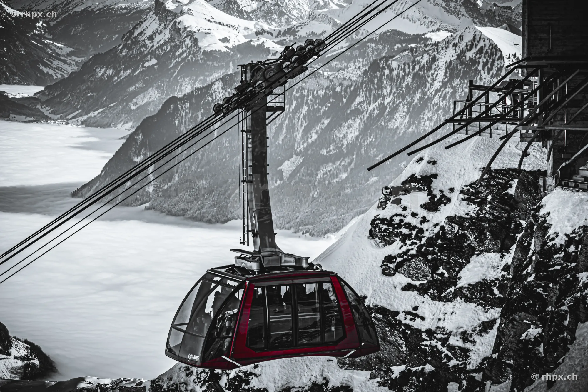 Rote Luftseilbahn vor verschneiter Bergkulisse über dem Nebelmeer
