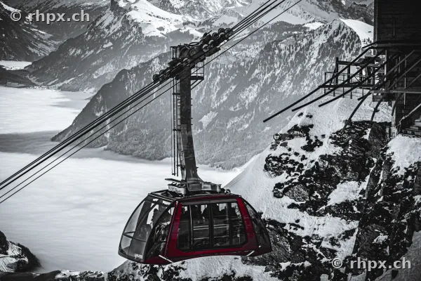 Rote Luftseilbahn vor verschneiter Bergkulisse über dem Nebelmeer