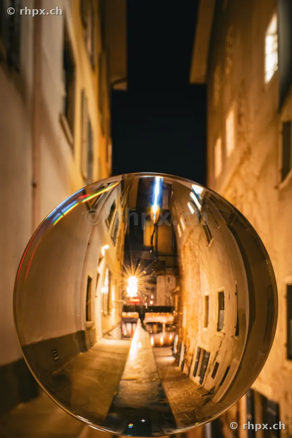 View of a nocturnal alley in Lucerne's old town through a glass sphere