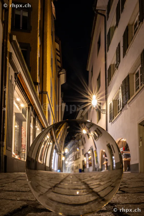 A glass sphere resting on the cobblestones of a dark alley in the Lucerne Old Town at night