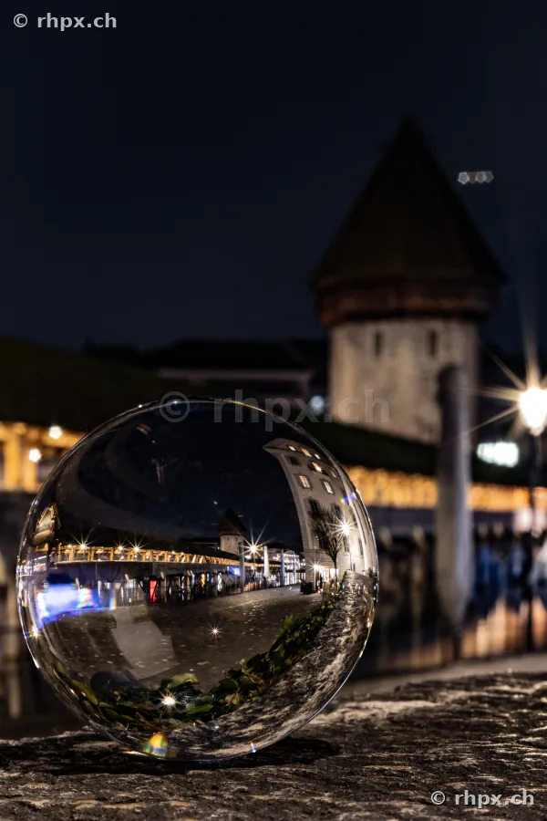 Night view of the Chapel Bridge in Lucerne reflected in a glass sphere