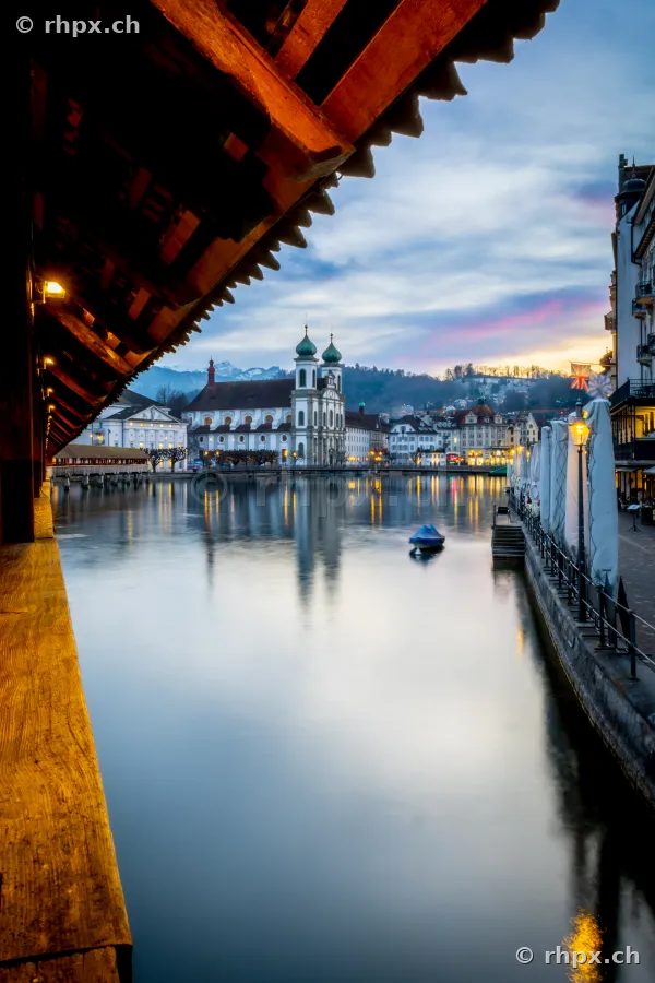 View from inside the Chapel Bridge across the Reuss river towards the Jesuit Church in Lucerne at dusk