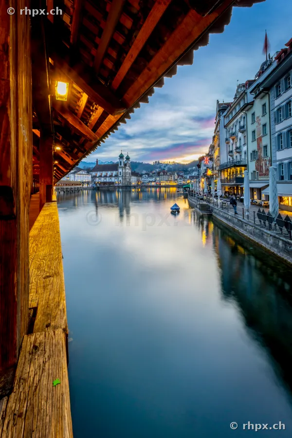 View from the covered Chapel Bridge looking out over the Reuss river and the Jesuit Church in Lucerne at dusk.