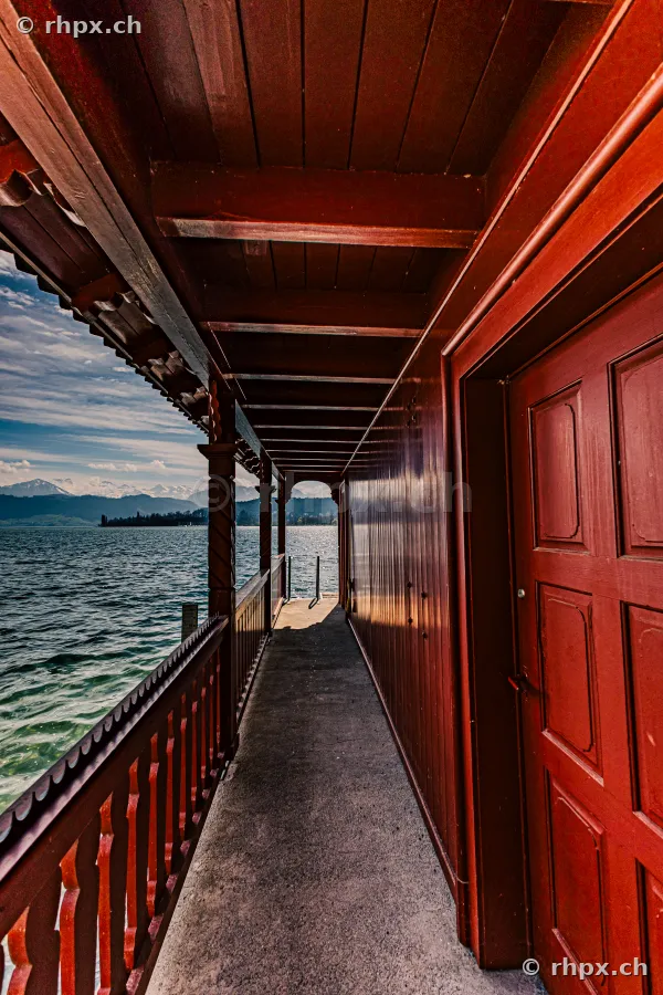 Covered wooden walkway of a historic vessel or building overlooking Lake Lucerne