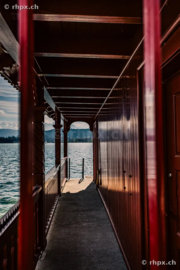 View through a covered wooden walkway towards Lake Lucerne with the Alps in the background