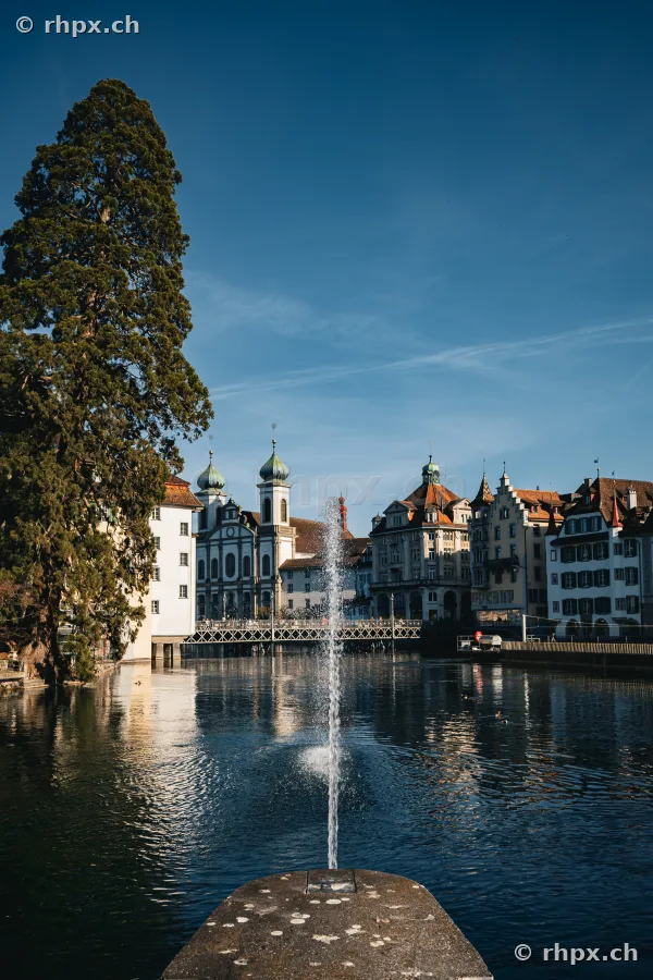 View across a fountain onto the Reuss river with the Jesuit Church in Lucerne