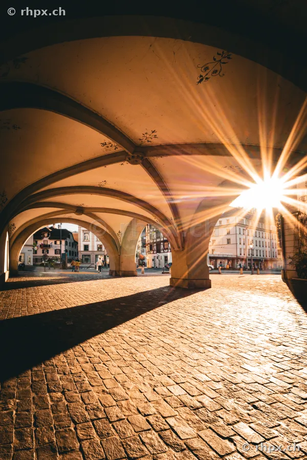 Tiefstehende Sonne wirft Strahlen unter die historischen Laubengänge am Weinmarkt in Luzern