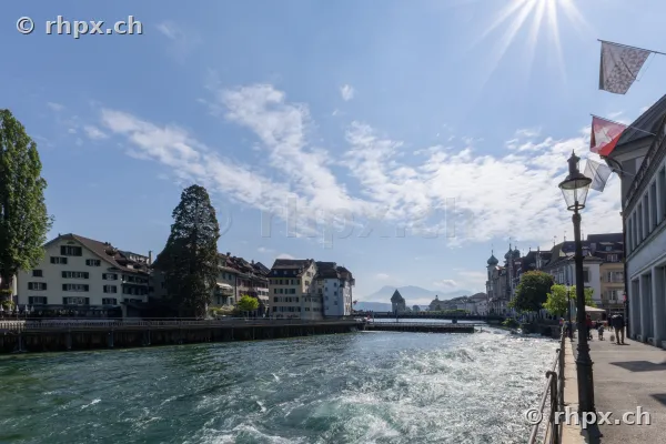 Blick auf den Fluss Reuss in Luzern mit historischen Gebäuden und den Bergen im Hintergrund